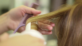 ヘアアイロンで髪を巻く美容師